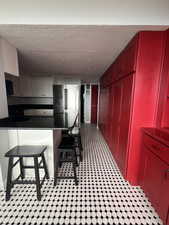 Kitchen with freestanding refrigerator, a textured ceiling, granite countertops, black microwave, and red cabinetry