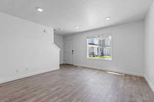 Unfurnished room with a textured ceiling, wood finished floors, baseboards, and recessed lighting
