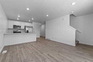 Kitchen featuring appliances with stainless steel finishes, baseboards, a peninsula, white cabinetry, and open floor plan