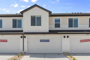 Townhome / multi-family property with board and batten siding, an attached garage, driveway, and roof with shingles