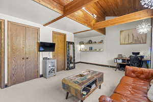 Living area with carpet floors, wooden ceiling with exposed beams, an office area, and baseboards