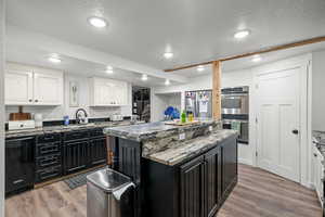 Kitchen featuring appliances with stainless steel finishes, dark cabinetry, light wood-style floors, a textured ceiling, and recessed lighting