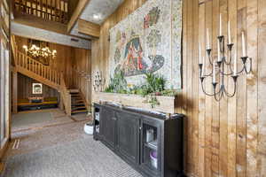 Carpeted living room featuring wooden walls, a chandelier, and stairway