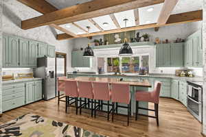 Kitchen with stainless steel appliances, green cabinets, beamed ceiling, light wood-type flooring, and light countertops