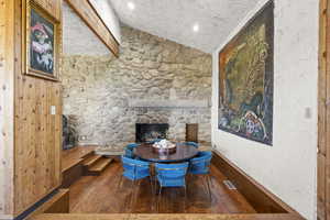 Dining space with vaulted ceiling, hardwood / wood-style flooring, a stone fireplace, and baseboards