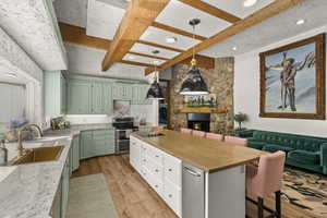 Kitchen with green cabinets, double oven range, a sink, a stone fireplace, and light wood finished floors