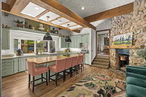 Kitchen with green cabinets, beam ceiling, light countertops, light wood-style flooring, and hanging light fixtures