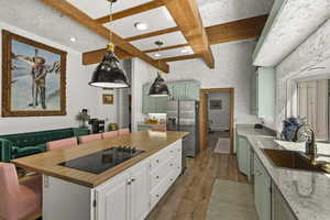 Kitchen featuring green cabinets, a sink, stainless steel fridge, black electric cooktop, and light wood-type flooring