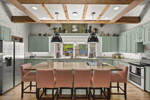 Kitchen with appliances with stainless steel finishes, green cabinets, light wood-style floors, beam ceiling, and light countertops