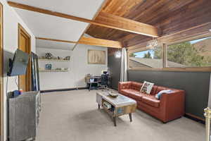 Carpeted living room with a chandelier, baseboards, and wood ceiling with exposed beams