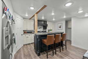 Kitchen featuring a textured ceiling, light wood-type flooring, stainless steel fridge, baseboards, and a kitchen bar
