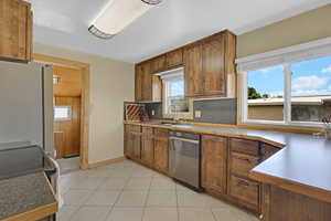Kitchen with stainless steel appliances, a sink, backsplash, light tile patterned floors, and brown cabinets