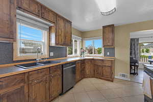 Kitchen featuring dishwashing machine, a sink, backsplash, and light tile patterned floors