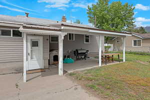 Rear view of house with a lawn, metal roof, a chimney, and a patio