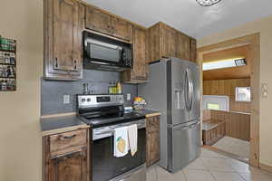 Kitchen with stainless steel appliances, light tile patterned floors, dark countertops, and tasteful backsplash