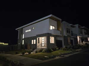 Contemporary house featuring stone siding, a balcony, and stucco siding