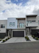 Modern home featuring stone siding, a balcony, stucco siding, and an attached garage