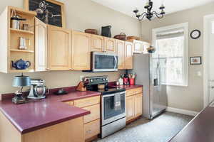 Kitchen with stainless steel appliances, light brown cabinetry, open shelves, a chandelier, and baseboards