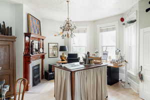 Home office with light wood-style flooring, a chandelier, a tile fireplace, and a textured ceiling