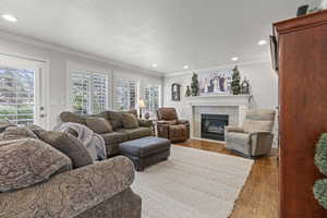 Living area featuring ornamental molding, recessed lighting, a tiled fireplace, light wood-type flooring, and a textured ceiling