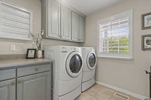 Washroom with cabinet space, independent washer and dryer, baseboards, and light tile patterned floors