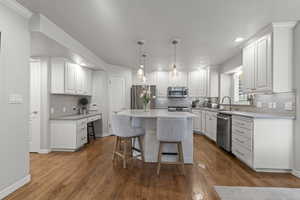 Kitchen with stainless steel appliances, a sink, a kitchen bar, white cabinetry, and decorative backsplash