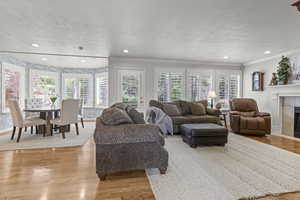 Living room with a textured ceiling, ornamental molding, a fireplace, light wood-style floors, and recessed lighting