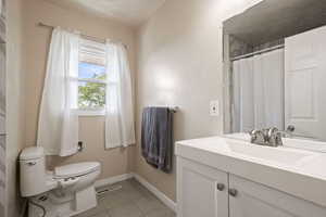 Full bath with toilet, vanity, tile patterned floors, and baseboards