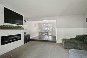 Living area with carpet flooring, a glass covered fireplace, a decorative wall, and wainscoting