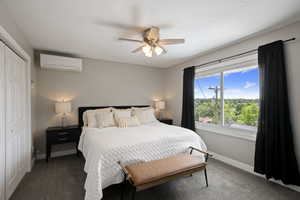 Carpeted bedroom featuring a wall mounted air conditioner, baseboards, a closet, and ceiling fan