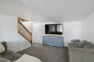 Carpeted living area featuring baseboards, stairway, and a textured ceiling