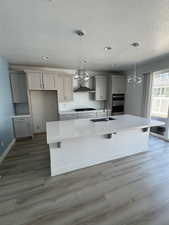 Kitchen featuring a sink, wall chimney exhaust hood, a large island, wood finished floors, and gray cabinets
