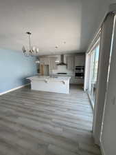 Kitchen featuring wall chimney range hood, a sink, black gas stovetop, an island with sink, and light countertops