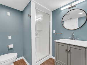 Full bathroom featuring baseboards, wood finished floors, a shower stall, vanity, and toilet