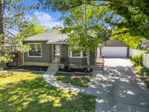 View of front facade featuring a garage, roof with shingles, concrete driveway, and an outbuilding