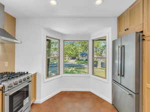 Kitchen with high end appliances, wall chimney range hood, healthy amount of natural light, tile patterned floors, and recessed lighting