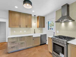 Kitchen with wall chimney exhaust hood, stainless steel appliances, backsplash, a sink, and light countertops