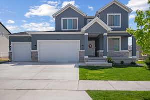 View of front of home featuring stone siding, stucco siding, a front lawn, and concrete driveway