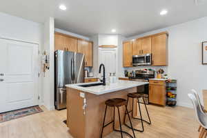 Kitchen featuring stainless steel appliances, a sink, a breakfast bar, light wood-style floors, and recessed lighting