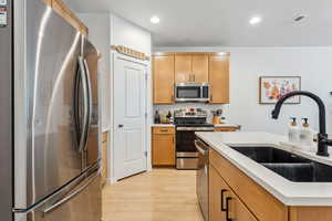 Kitchen with appliances with stainless steel finishes, a sink, light wood-type flooring, light countertops, and recessed lighting