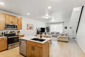 Kitchen featuring stainless steel appliances, a sink, light countertops, light wood-style flooring, and an island with sink
