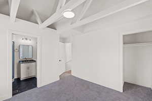 Unfurnished bedroom with a sink, dark carpet, a closet, ensuite bathroom, and baseboards