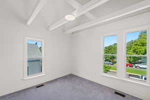 Carpeted spare room with plenty of natural light, baseboards, and beamed ceiling