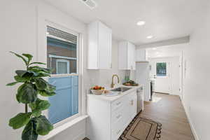 Kitchen featuring a sink, stainless steel dishwasher, light wood-style floors, white cabinets, and recessed lighting