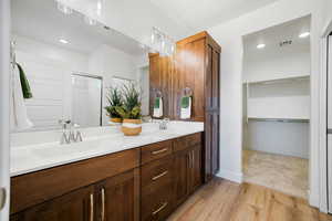 Bathroom featuring wood finished floors, double vanity, a shower with shower door, a spacious closet, and baseboards