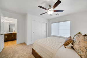 Bedroom featuring light carpet, a closet, baseboards, ceiling fan, and ensuite bath