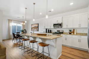 Kitchen with stainless steel appliances, light wood-style floors, a breakfast bar area, white cabinetry, and recessed lighting