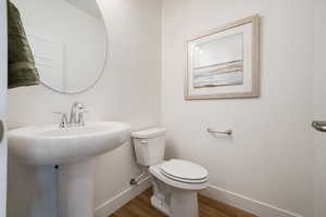Bathroom featuring baseboards, wood finished floors, toilet, and a sink