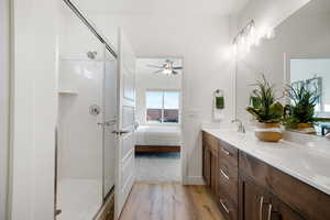 Bathroom with wood finished floors, a shower stall, ceiling fan, double vanity, and connected bathroom