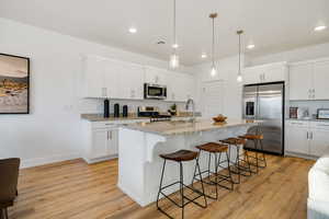 Kitchen featuring stainless steel appliances, a sink, light wood-type flooring, a kitchen bar, and recessed lighting